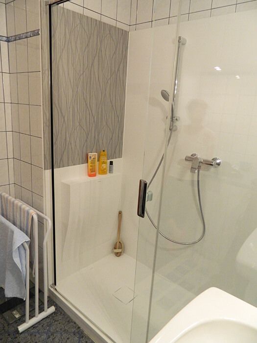 Renoviertes Badezimmer mit moderner, barrierefreier Duschkabine, weißen Wandfliesen, grauem Duschbereich.